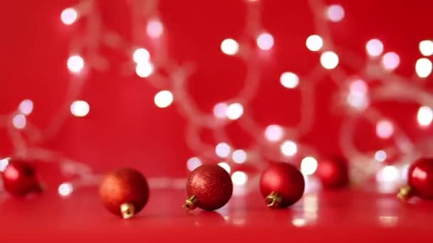 Czerwone świąteczne kulki toczą się na czerwonym tle. Girlanda świąteczna błyszczy w tle - Materiał filmowy, wideo
