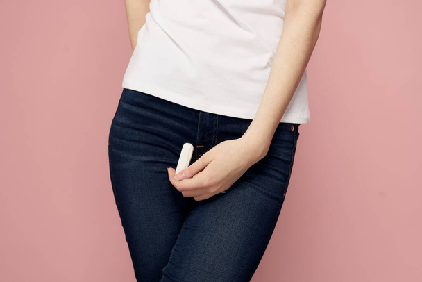 Woman with a tampon in her hand critical days hygiene white t-shirt jeans pink background menstrual cycle - Valokuva, kuva