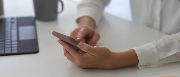 Close up view of female hands using smartphone on white table in workplace - Foto, afbeelding