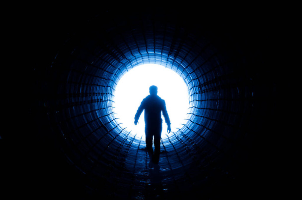 Büyük bir tünelin sonunda ışığa doğru yürüyen bir adamın silüeti. Kaçış, çıkış, özgürlük, klinik ölüm kavramı - Fotoğraf, Görsel