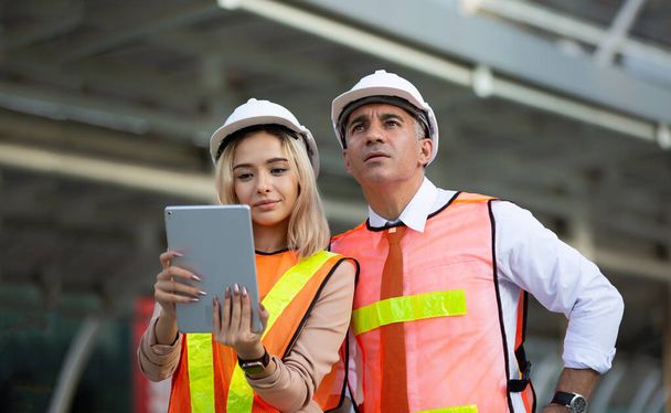 Vrouwelijke industrieel ingenieur draagt een witte helm terwijl hij op een bouwplaats staat met zakenman in gesprek over werkplan, Ingenieur en architecten op bouwplaats concept - Foto, afbeelding