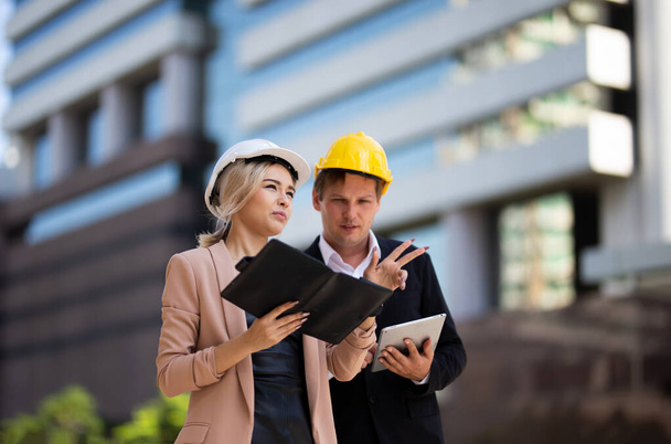 Female industrial engineer wearing a white helmet while standing in a construction site with businessman talking on working plan, Engineer and architects at construction site concept - Photo, Image