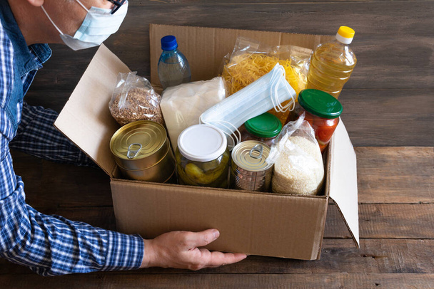 Pudełko kartonowe z masłem, konserwami, płatkami zbożowymi i makaronem. Pudełko darowizn z różnymi przedmiotami żywnościowymi. Ręce są umieszczone jedzenie. - Zdjęcie, obraz
