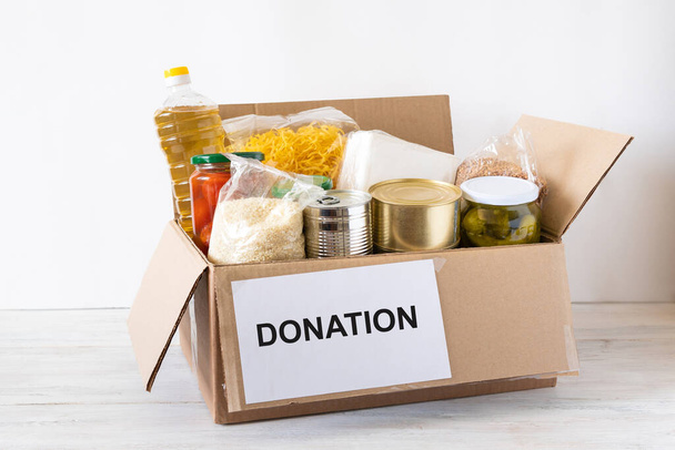 Donation box with various food. Open cardboard box with oil, canned food, cereals and pasta. - Фото, изображение