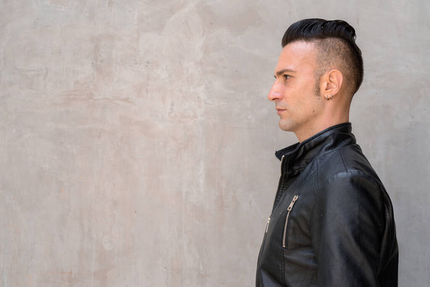 Vista de perfil de joven italiano guapo con undercut usando chaqueta de cuero negro - Foto, Imagen