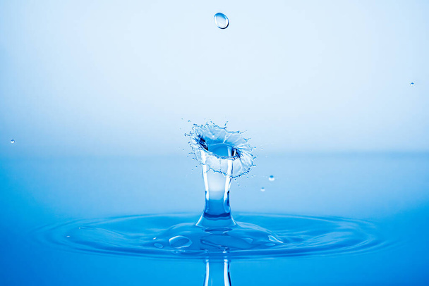 Wassertropfen plätschern in die blaue Wasseroberfläche. Gesundheits- und Reinheitskonzept - Foto, Bild