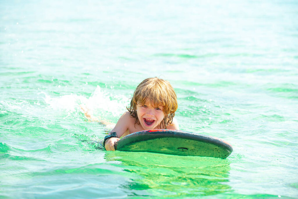 Kid boy swimming with surfboard on the beach on blue sea in summer. Blue ocean with wawes. Child boy swimming in sea. - Φωτογραφία, εικόνα