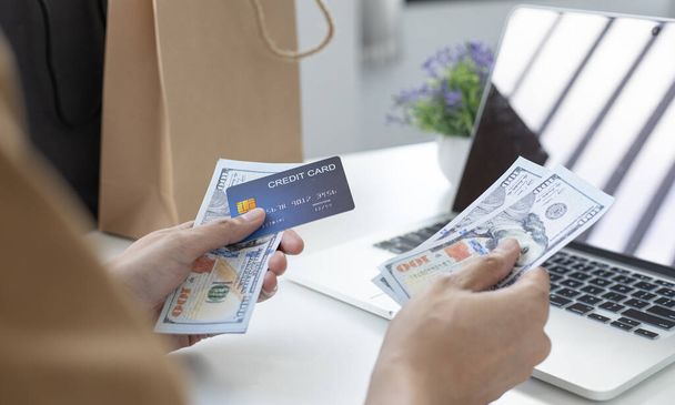 Jongeman heeft een creditcard in plaats van een dollarbiljet om online te winkelen via internet, met behulp van een creditcard in plaats van contant geld concept. - Foto, afbeelding
