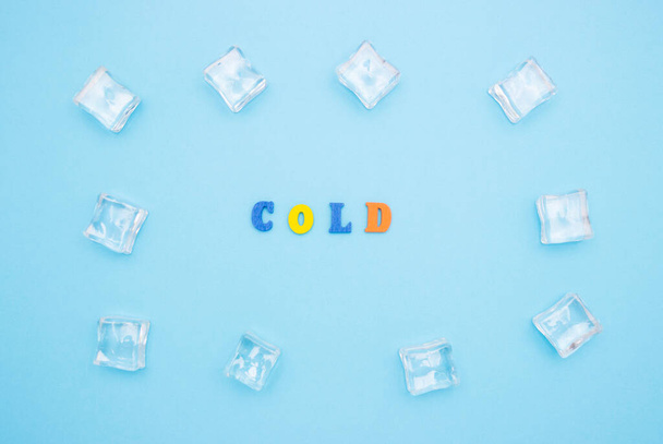 Het woord COLD op een blauwe achtergrond van houten veelkleurige letters, ijsblokjes rond het woord. - Foto, afbeelding