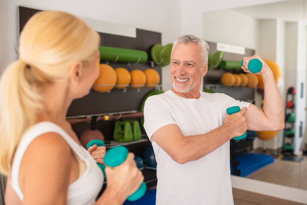 Grey-haired bearded man showing his biceps to a woman and smiling - Foto, afbeelding