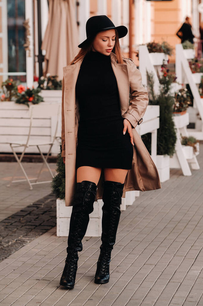 Stylish young woman in a beige coat in a black hat on a city street. Women's street fashion. Autumn clothing.Urban style. - Fotoğraf, Görsel