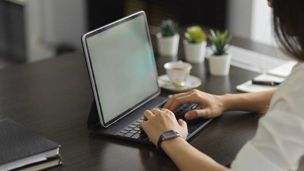 Vue latérale des mains féminines travaillant avec une tablette numérique sur un bureau avec des décorations et des fournitures - Photo, image