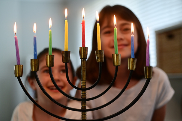 Dvě šťastné židovské sestry při pohledu a zpěvu na krásnou menorah svícen zářící na osm dní židovského svátku Chanuka. - Fotografie, Obrázek