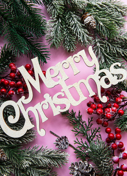 Branches of a Christmas tree and decorations on a pink pastel background with the wishes of Merry Christmas - Foto, imagen