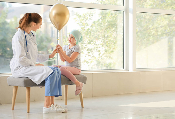 Доктор и маленькая девочка с золотым шариком в клинике. Концепция информированности детей о раке - Фото, изображение