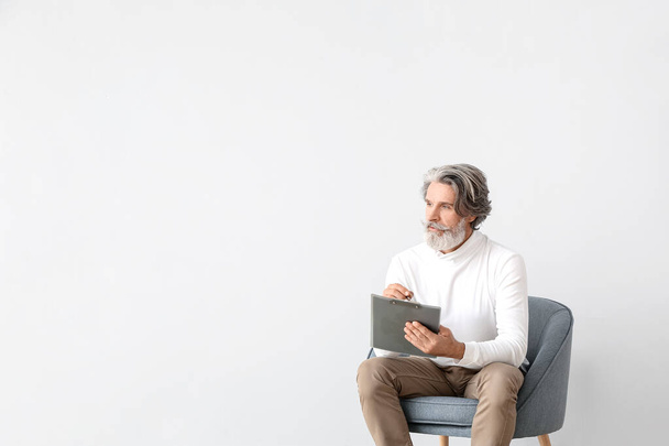 Senior mannelijke psycholoog zit in fauteuil op lichte achtergrond - Foto, afbeelding