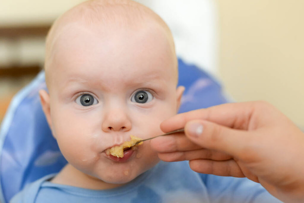 Mom feeds her funny son from a spoon with applesauce - Foto, Bild