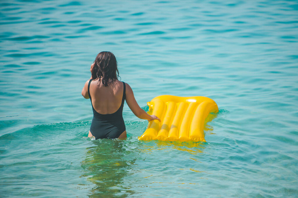 жінка з жовтим надувним матрацом, що йде до моря літні канікули вид ззаду
 - Фото, зображення