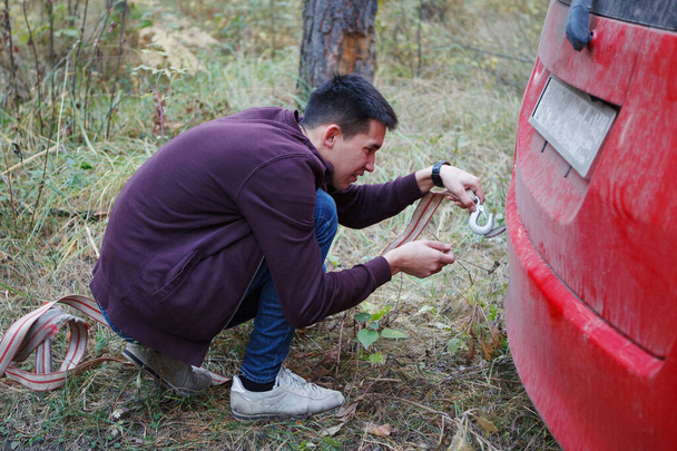 Young man repairs the rear bumper of a red car in the woods. - Photo, Image