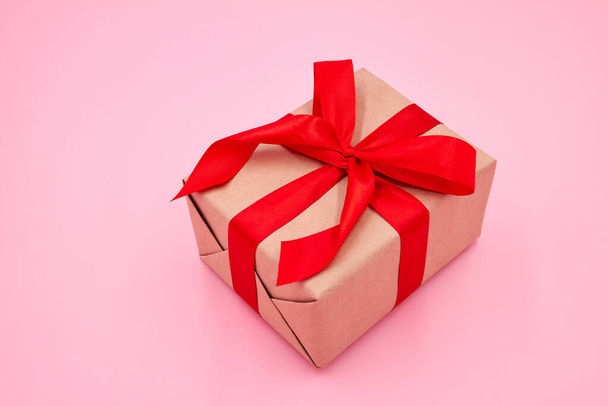Рождественская или новогодняя подарочная коробка с красной лентой на розовом фоне. Крупный план, избирательный фокус - Фото, изображение