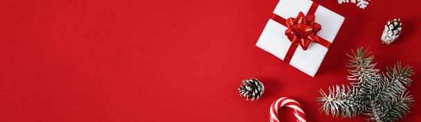 Christmas composition. Gift box with festive ribbon and christmas decorations on red background with a copy space, top view - Photo, image