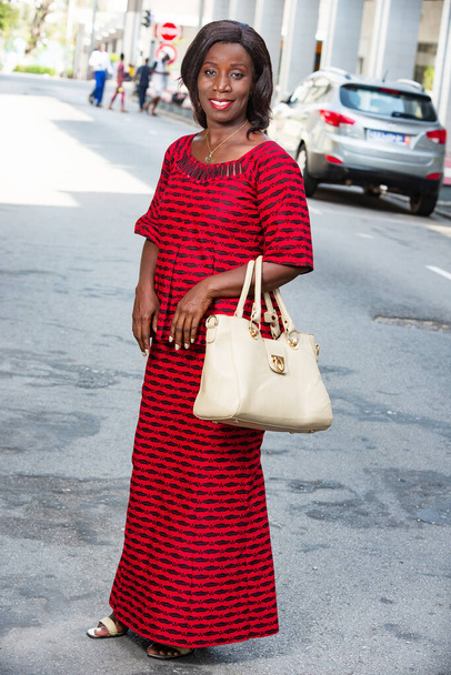 maturo africano donna in piedi all'aperto guardando fotocamera sorridente con borsetta. - Foto, immagini
