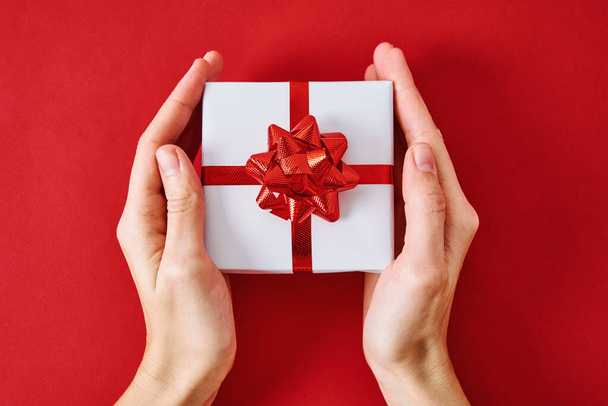 Gift with festive ribbon in a woman hands on red background, top view - Photo, Image