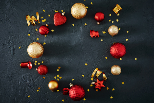 Composizione natalizia. Cornice rotonda fatta di palline di Natale rosse e dorate e nastri festivi su uno sfondo scuro, vista dall'alto - Foto, immagini