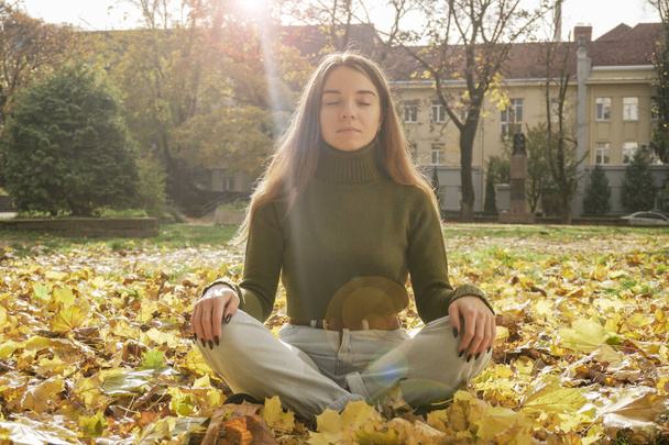 Beautiful young girl meditating in autumn park. woman meditates in the forest in sunny day - Photo, Image