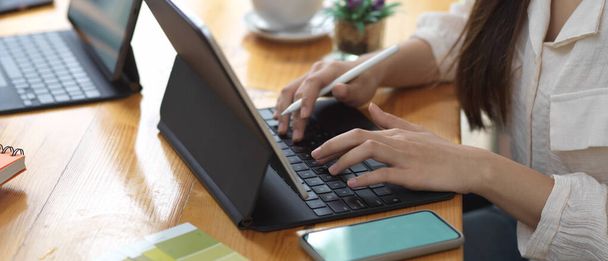 Vista lateral de las manos femeninas escribiendo en el teclado de la tableta y trabajando con el teléfono inteligente de la maqueta  - Foto, Imagen