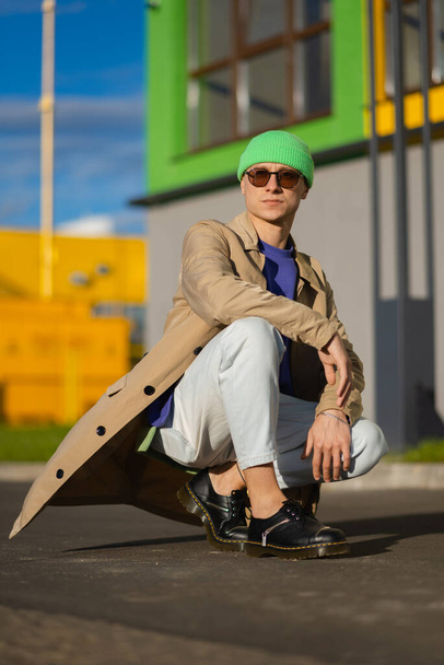 Un joven con un abrigo beige y un sombrero verde en la ciudad - Foto, imagen