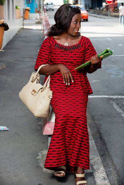beautiful african adult woman sitting in red loincloth on the street, holding in hand a green document with a beautiful looking sourrie side - Fotó, kép