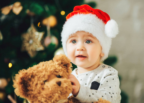 Baby with Teddy bear in hands, Christmas tree in the background.  - Foto, Imagem