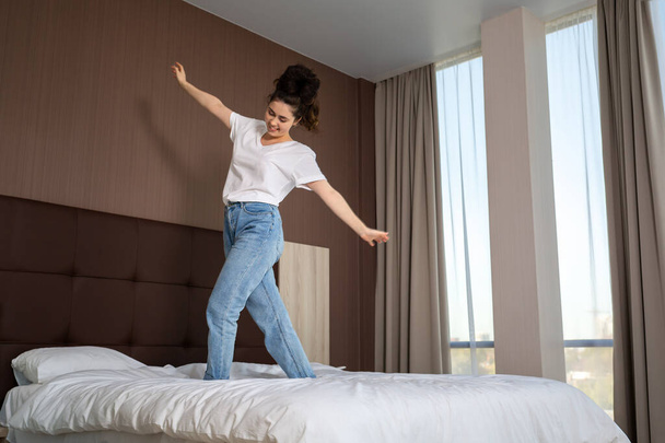 Yatak odasındaki yatakta gündelik kıyafetlerle dans eden mutlu genç kadın. Alt görünüm. - Fotoğraf, Görsel
