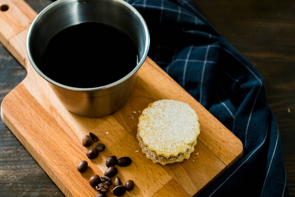 Italienisch-amerikanischer schwarzer Kaffee in einer Vintage-Tasse mit Kaffeebohnen herum und einem handgemachten Plätzchen mit Zucker und einer Mokka-Kanne dahinter. Alles in Vintage-Holz-Hintergrund und es ist ein gesundes und leckeres Frühstück. - Foto, Bild