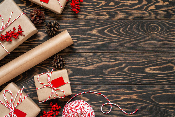 クリスマスプレゼントを包む。茶色の木製の背景に装飾された贈り物、双子の文字列、クラフト紙と松のコーンでフラットレイアウト。コピースペース。トップ表示. - 写真・画像