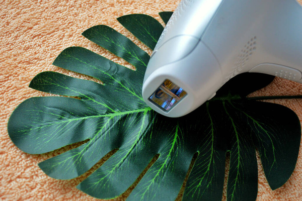 Фотоэпилятор лежит на пальмовом листке на фоне бежевой ткани. - Фото, изображение