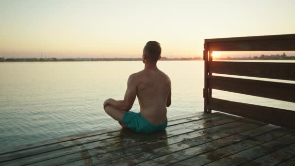 若い男が桟橋の端に座って瞑想している。美しい夕日。4K - 映像、動画