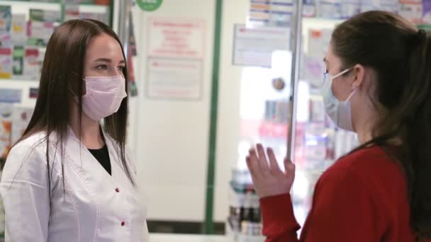 Eczacı ve müşteri eczanede iletişim kuruyor. Tıbbi maskeli kadınlar. Alıcının omzunun üstünden bak. Virüs salgını ve enfeksiyona karşı koruma kavramı - Video, Çekim