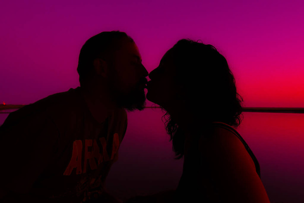 Fiatal házaspár sziluettben csókolóznak naplementekor a tenger felett. a szerelem, a szeretet és a romantika fogalma - Fotó, kép