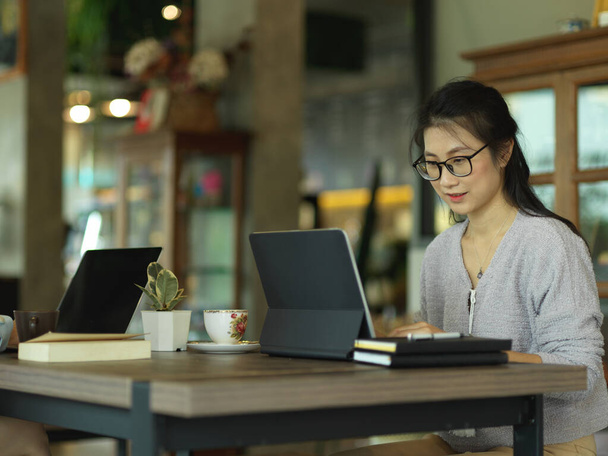 Widok boczny freelancerki pracującej z tabletem cyfrowym i artykułami piśmiennymi w miejscu pracy - Zdjęcie, obraz