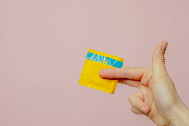 Female hand holding condom on pink background. Top view. The concept of sexual preservation. High quality photo - Photo, Image