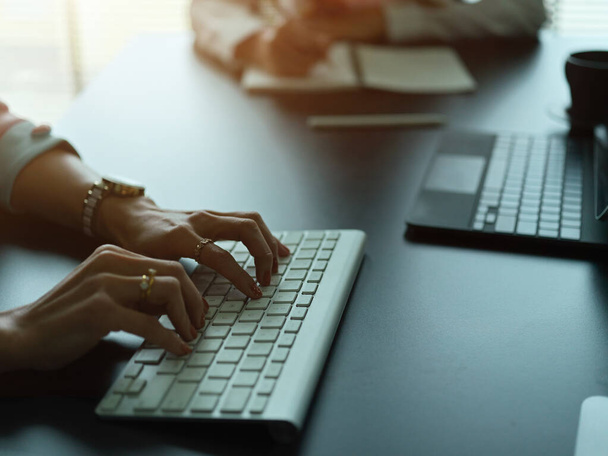Vue latérale des mains féminines tapant sur le clavier d'ordinateur sans fil sur le bureau - Photo, image