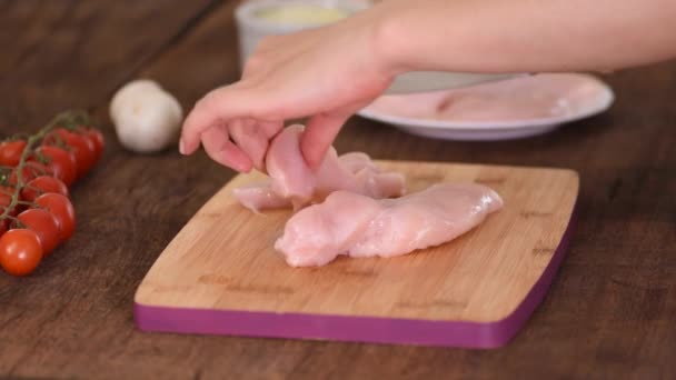 Female hands cutting chicken fillet on wooden chopping board. - Felvétel, videó