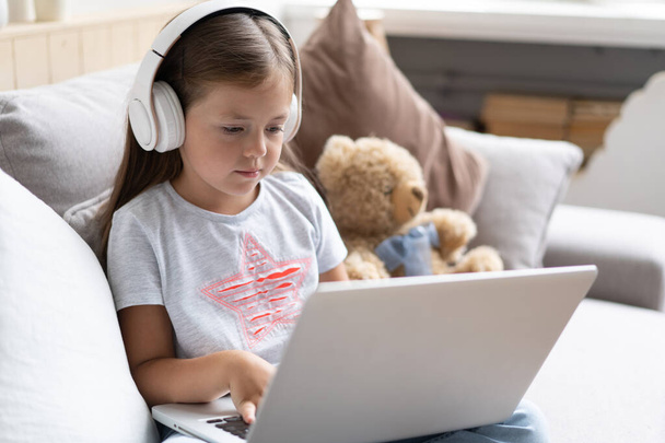Online education. Sweet girl with headphones looking video lesson teacher conference laptop sitting on the couch at home - Foto, Imagen