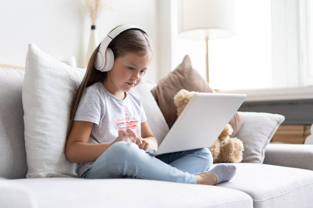 Online education. Sweet girl with headphones looking video lesson teacher conference laptop sitting on the couch at home - Foto, imagen