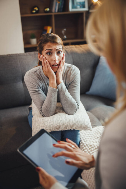 Aufnahme einer gestressten jungen Frau, die mit ihrer Psychotherapeutin diskutiert, während sie auf einem Sofa im Wohnzimmer sitzt. - Foto, Bild