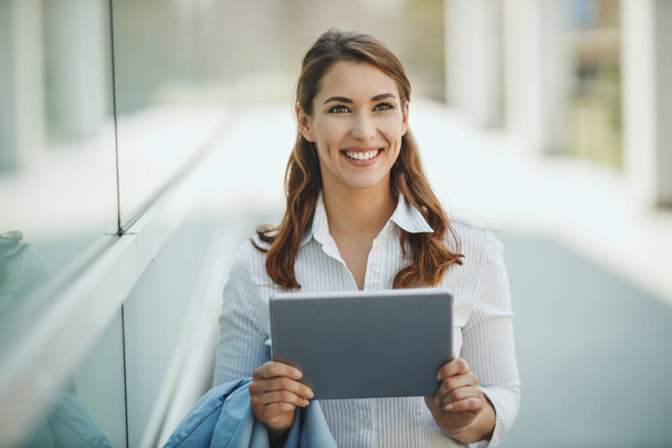 Prise de vue d'une jeune femme d'affaires tenant une tablette numérique et sortant d'un immeuble de bureaux pendant la pause. - Photo, image