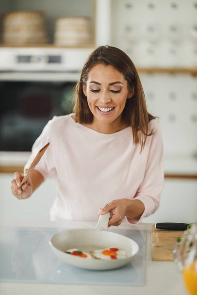 Aufnahme einer jungen Frau, die in ihrer Küche ein Spiegelei zum Frühstück zubereitet. - Foto, Bild