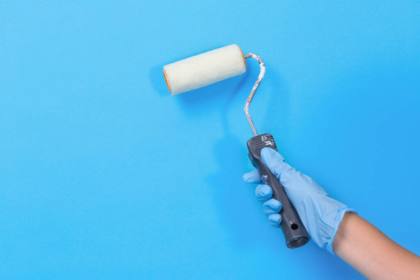 Hand with a roller for painting walls, blue background, place for text. home repair - Foto, Imagem